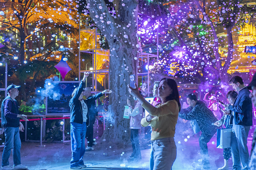 People interact with bubbles that glow under light installations in Jing'an District, Shanghai, China on April 29, 2025. /VCG